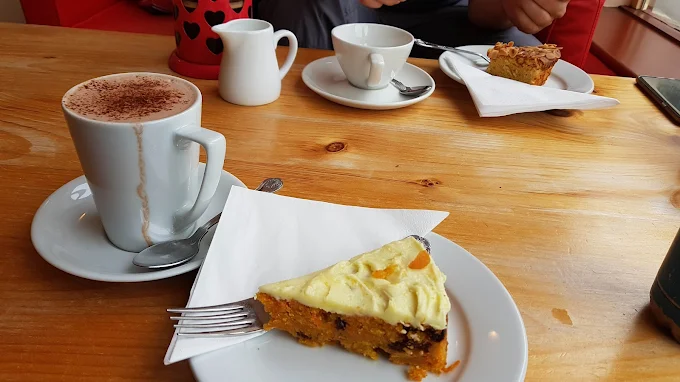 Flat white coffee with latte art beside a slice of orange and almond cake on a wooden table
